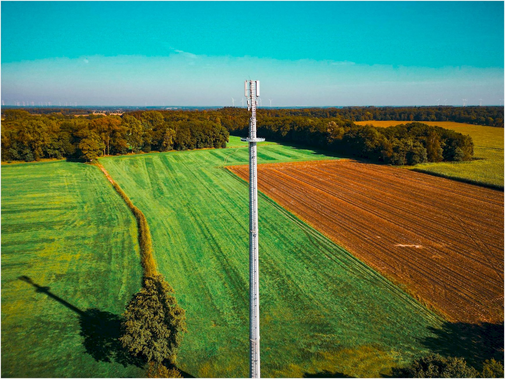 Aerial view of a telecom tower in a vibrant green field surrounded by forests.