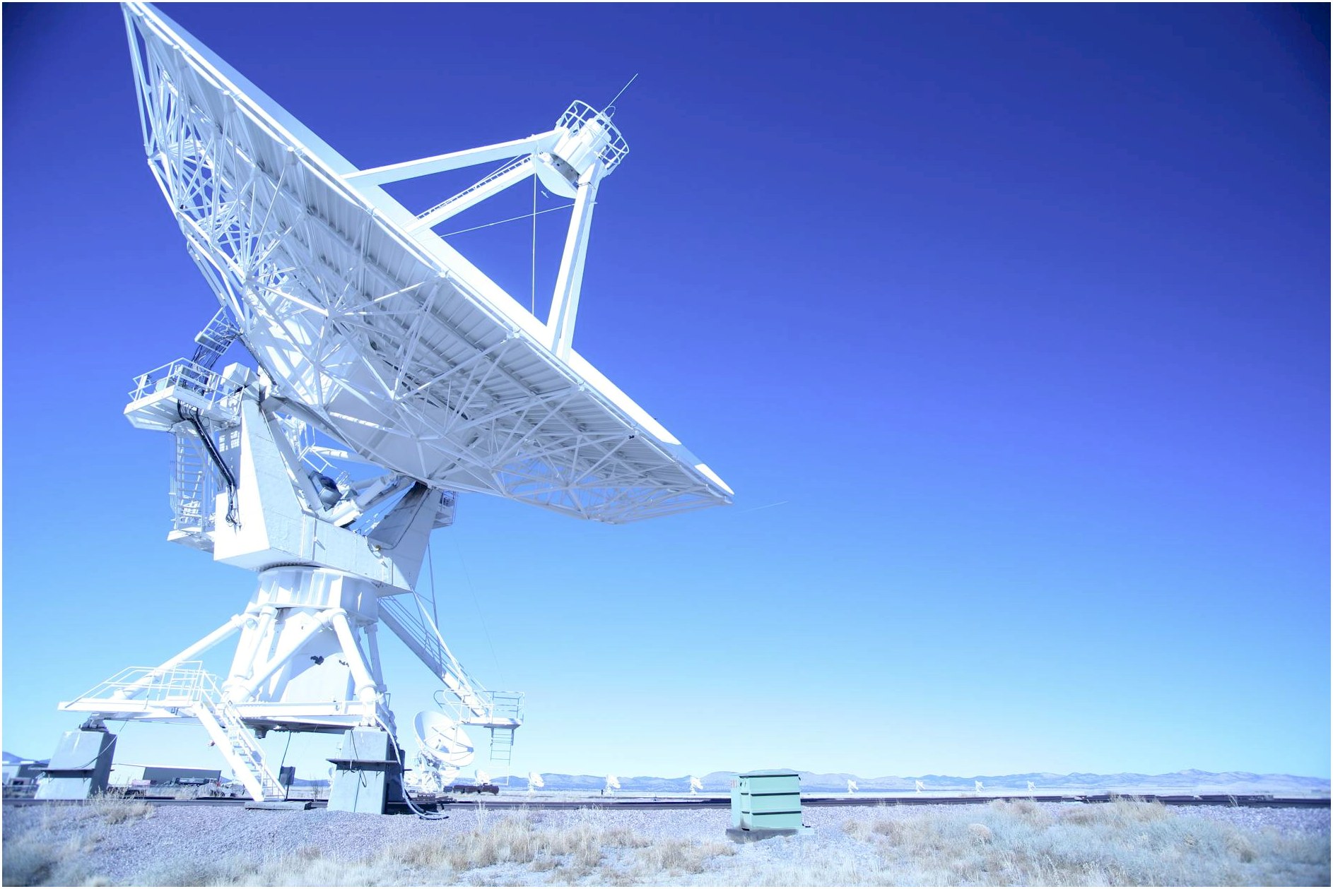 A large satellite dish observatory against a clear blue sky in a desert landscape, capturing signals.