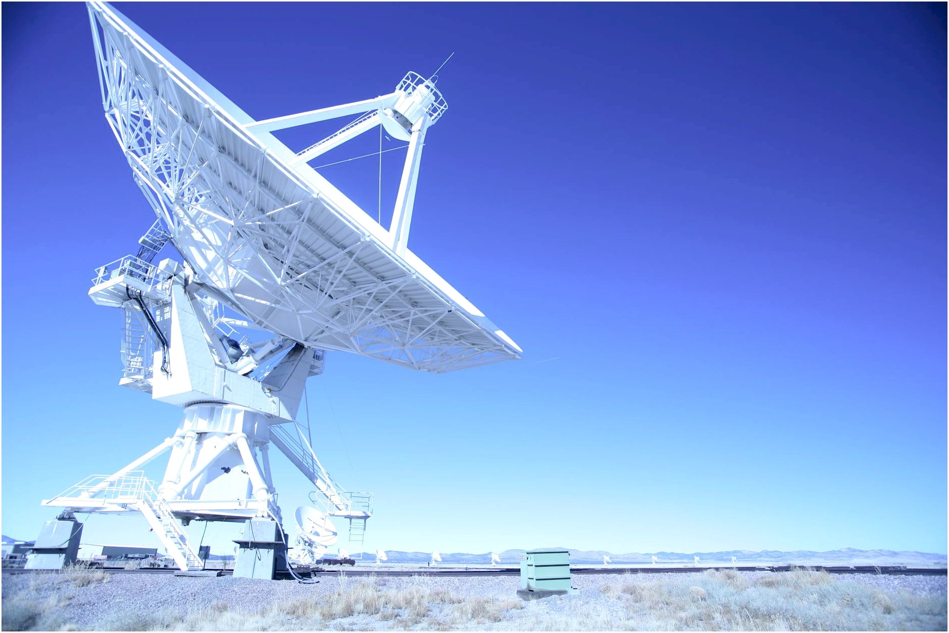 A large satellite dish observatory against a clear blue sky in a desert landscape, capturing signals.