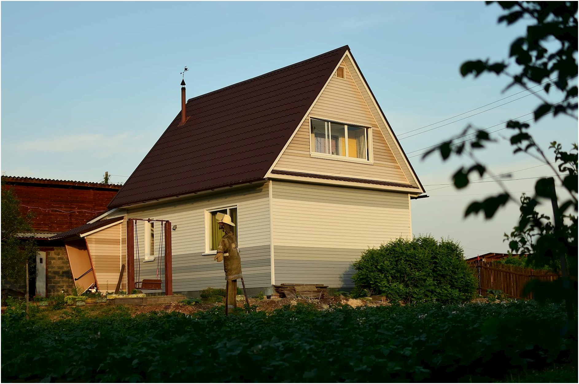 A suburban house with garden and scarecrow under warm evening sunlight, showcasing rustic charm.