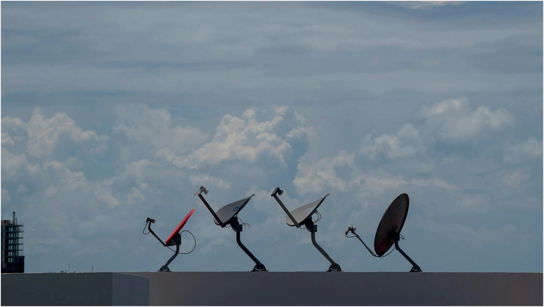 Four satellite dishes on a rooftop against a cloudy sky in Cancún, Mexico.